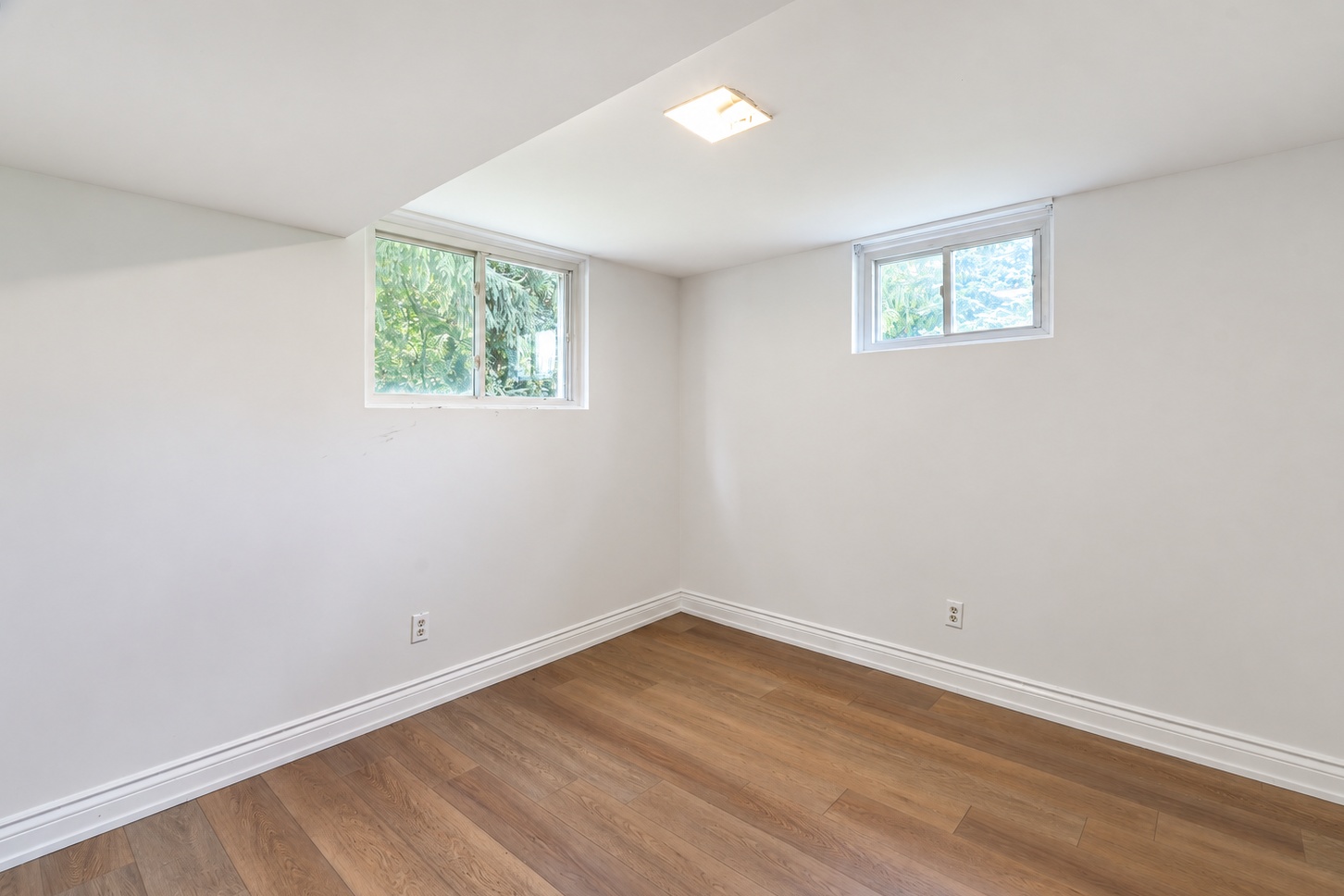 Basement room with two windows and warm-toned flooring